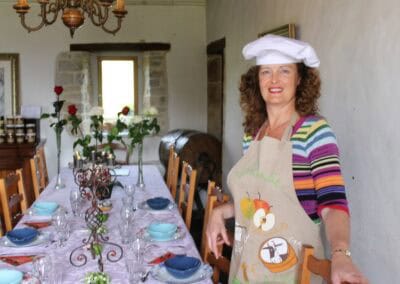 Table d'hôtes Bayeux at La Ferme Manoir Saint Barthélemy, featuring a woman in a chef's hat and a beautifully set table.
