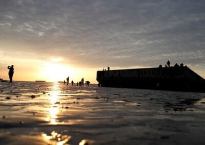 Silhouetted figures on a Mulberry harbour section at sunset, Normandie. L'Histoire du Débarquement et de la Bataille de Normandie.
