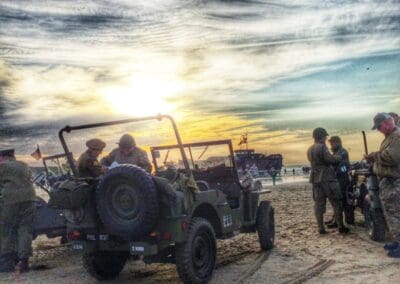 WWII reenactors and jeep on Normandy beach at sunset, a scene reminiscent of L'Histoire du Débarquement et de la Bataille de Normandie.