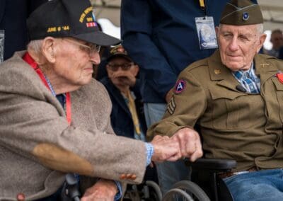 Two WWII veterans shaking hands at a D-Day event in Normandie, related to L'Histoire du Débarquement et de la Bataille de Normandie.