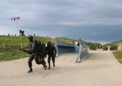 Normandy landing memorial featuring soldier statues and a landing craft replica. L'Histoire du Débarquement et de la Bataille de Normandie.